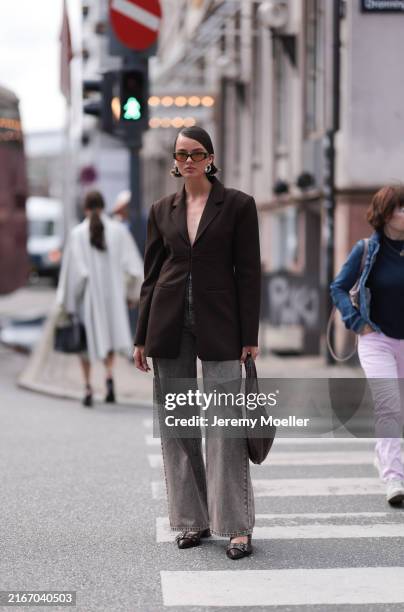Fashion Week guest is seen wearing oval black sunglasses with wide temples and orange lenses, abstract silver hoop earrings, a dark brown waisted...