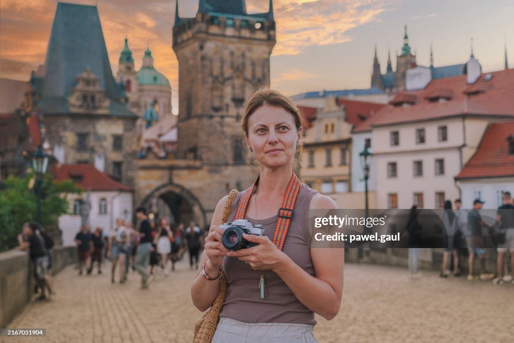 Woman taking pictures of Charles bridge during sunset Prague, Czech Republic