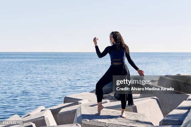young woman dancing on concrete blocks by the sea - contemporary dance stock pictures, royalty-free photos & images