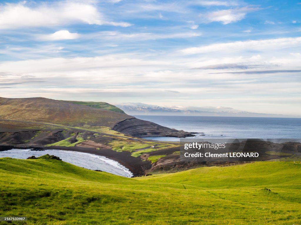Rocky coastline of Heimaey at sunset, with a black sand beach, a country road and a view on the Eyjafjallajokull (Eyjafjallajökull) glacier and volcano, Archipelago of the Westman Islands (Vestmannaeyjar) - South Iceland (Suðurland).