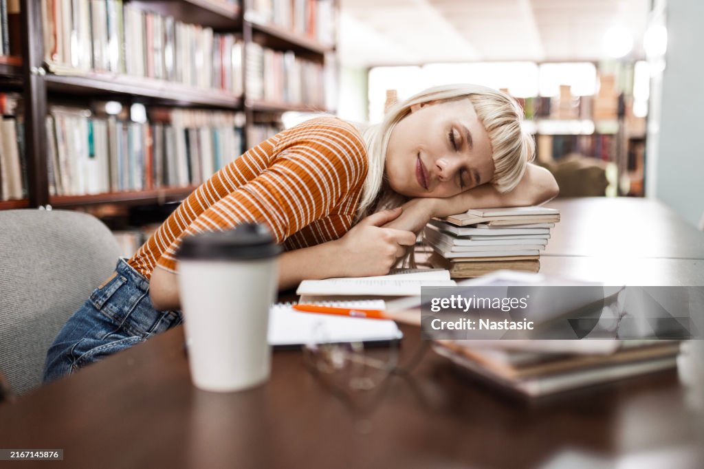 Tired female student sleeping at the library on a books