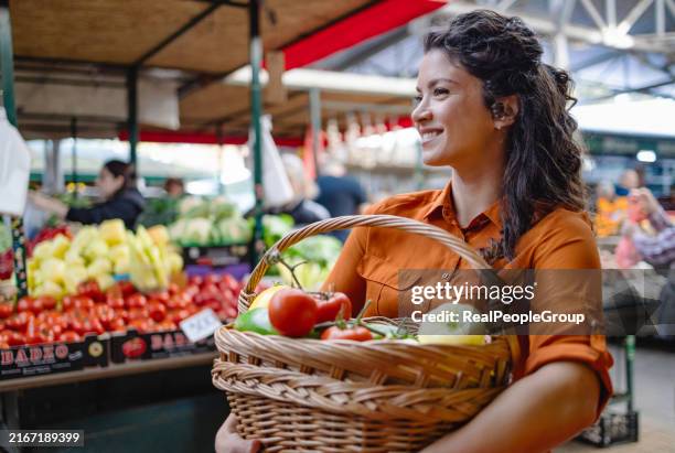 woman holding basket of vegetables at outdoor market. - mercado de produtos agrícolas imagens e fotografias de stock