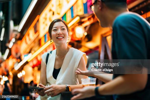 young asian couple enjoying their time sitting in illuminated narrow alleyway restaurants bars in downtown tokyo at night, chatting joyfully and having drinks after work. experiencing unique and authentic japanese atmosphere - japanese food stock pictures, royalty-free photos & images