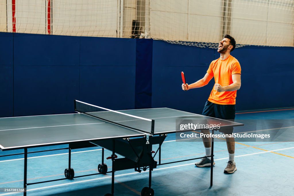 Energetic player showcasing precision serving in a table tennis match. The emphasis on the orange ball and racket captures the intensity of the sport