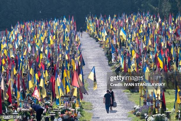People walk among graves at the Field of Mars cemetery in Lviv on August 24, 2024 to commemorate the fallen soldiers on the occasion of the...