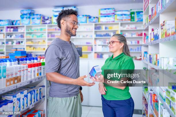 female pharmacist in a brazilian pharmacy offers medicine to a young customer while smiling in rio de janeiro - manaus stock pictures, royalty-free photos & images