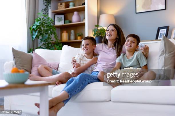 mother with sons on sofa enjoying home movie night. - parte de uma série imagens e fotografias de stock
