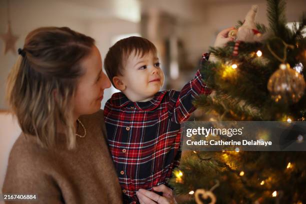 a mum decorating the christmas tree with her 18 month old baby boy in the arms - decorating the christmas tree stock pictures, royalty-free photos & images