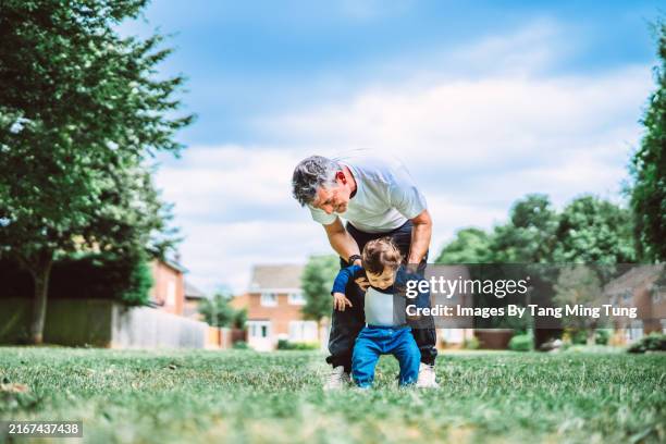 father helping his toddler son to walk in park joyfully - life events stock pictures, royalty-free photos & images