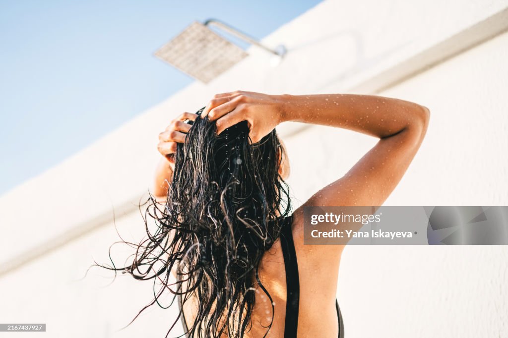 A beautiful unrecognizable woman washing hair in an outdoor shower