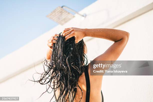 a beautiful unrecognizable woman washing hair in an outdoor shower - shampoo stockfoto's en -beelden
