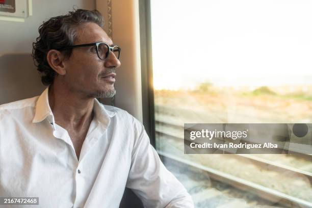 mature businessman sitting on a train looking out the window - reflection in train window stock pictures, royalty-free photos & images