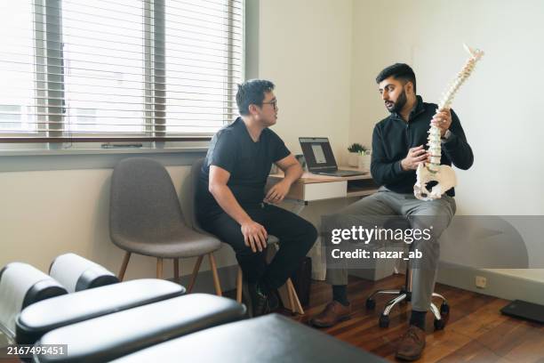 chiropractor explains patient using plastic model. - chiropractor stock pictures, royalty-free photos & images