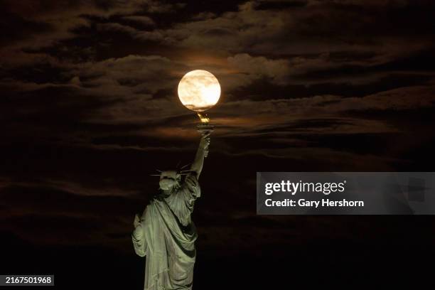 The Blue Sturgeon Supermoon rises out of clouds behind the Statue of Liberty in New York City on August 19 as seen from Jersey City, New Jersey.