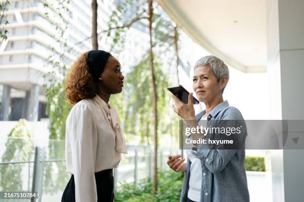 senior businesswoman using ai language translation app to communicate with her teammate - vertaling stockfoto's en -beelden