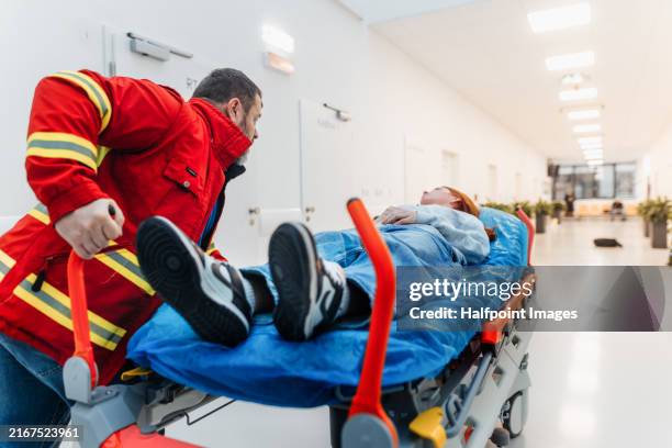 male paramedic in uniform pushing patient on stretcher across hospital corridor to emergency room. - trabajador de rescate fotografías e imágenes de stock