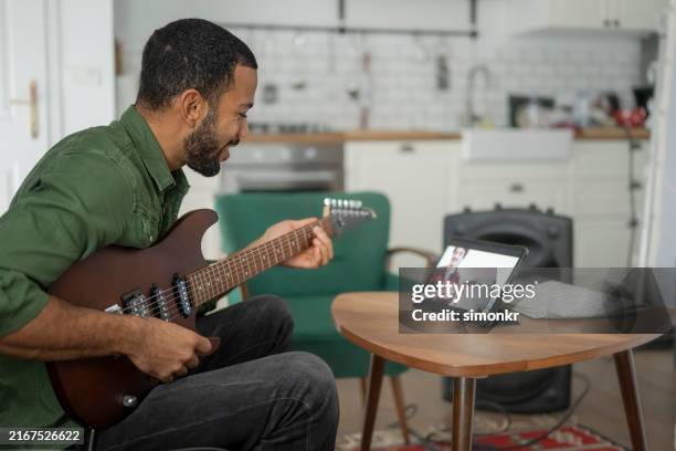 man learning to play guitar with tablet - mid adult men stock pictures, royalty-free photos & images
