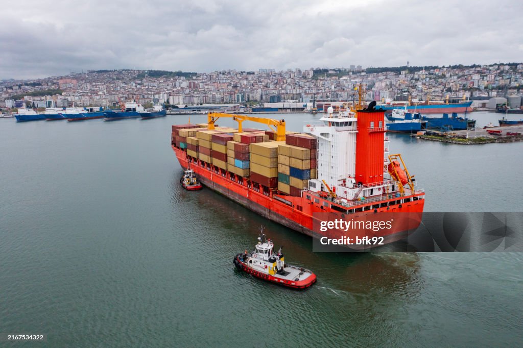 Aerial view of Cargo container ship carrying container and running with tugboat for import goods to cargo container terminal for customs. Concept of logistics transportation and shipping.