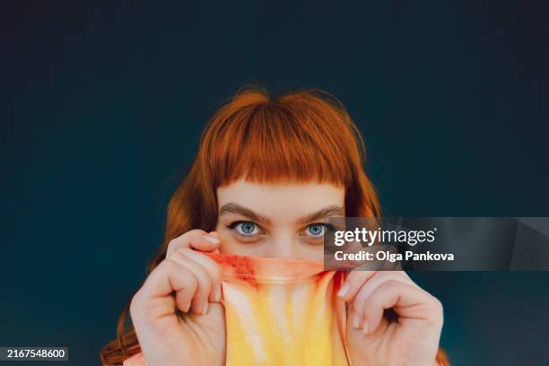 expressive red-haired young woman playfully hiding behind his t-shirt - flirter photos et images de collection