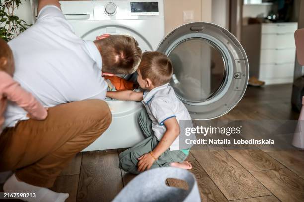 father and son do laundry together, bonding over household chores - lessive corvée domestique photos et images de collection