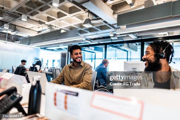 hombres jóvenes hablando y trabajando en el centro de llamadas en la oficina - espacio de trabajo virtual compartido fotografías e imágenes de stock
