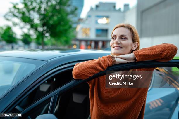 mujer alegre apoyada en su coche en la ciudad - lean fotografías e imágenes de stock