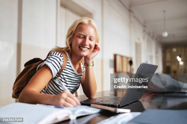 glücklicher universitätsstudent, der mit laptop in der bibliothek lernt - studentin stock-fotos und bilder