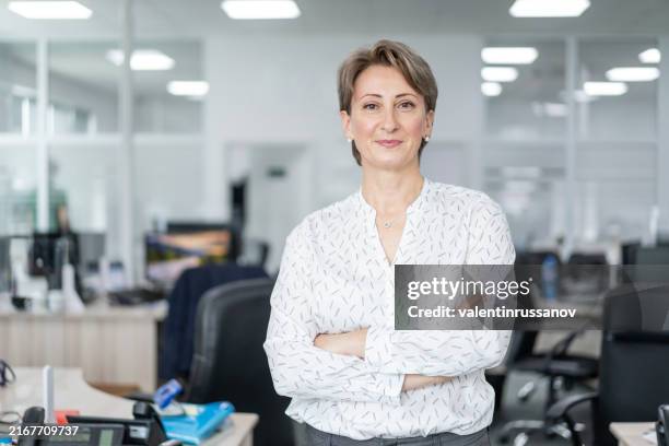 mujer con confianza parada sola en la oficina. - mujeres de mediana edad fotografías e imágenes de stock