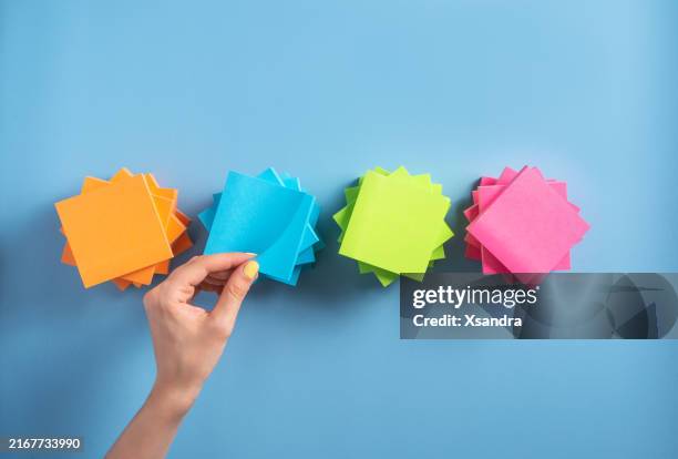 colorful sticky notes neatly stacked on a blue background, hand removing one note from the top - colour coordinated stock pictures, royalty-free photos & images