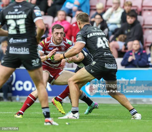 Wigan Warriors' Jake Wardle runs with the ball under pressure from Hull FC's Jed Cartwright during the Betfred Super League Round 23 match between...
