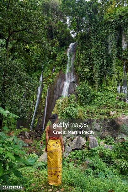 asian woman standing in front of waterfall set amongst lush tropical foliage, looking at view - sarong fotografías e imágenes de stock