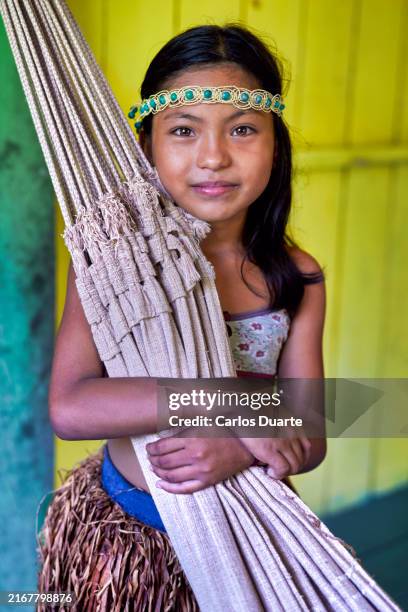 portrait en gros plan d’une belle fille indigène de l’amazonie au brésil dans sa robe traditionnelle étreignant son lit, qui est son hamac, et souriant à la caméra - amazon girl photos et images de collection
