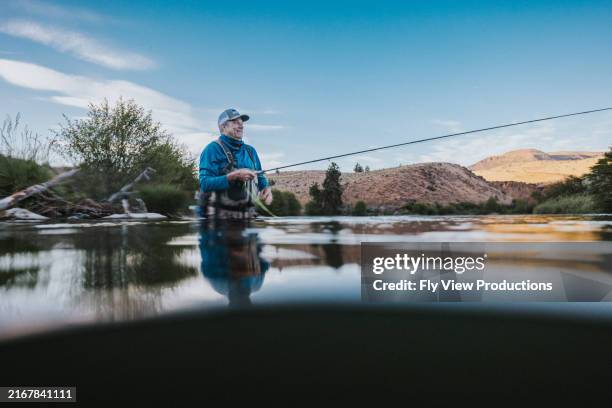 man stands waist deep in the river while fishing - casting stock pictures, royalty-free photos & images