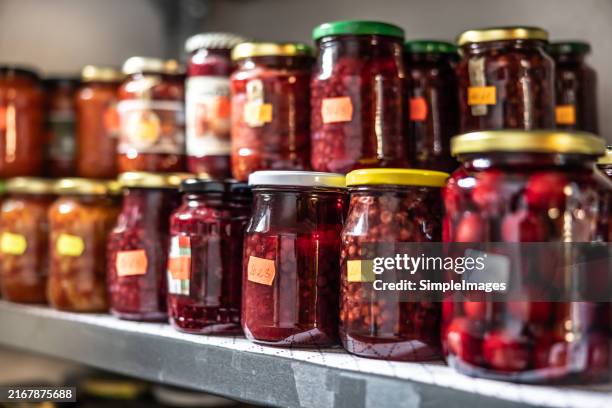 fruit and vegetable preserves in glass jars on a shelf in the pantry. - jam jar stock pictures, royalty-free photos & images
