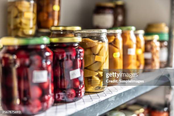 fruit and vegetable preserves in glass jars on a shelf in the pantry. - producto enlatado fotografías e imágenes de stock