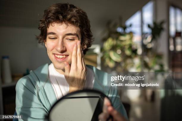 young man cleaning his face with a cotton cleaning pad at home - human head stock pictures, royalty-free photos & images