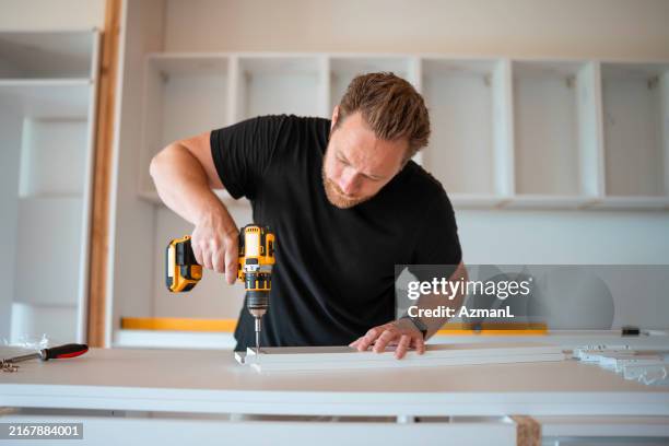 uomo adulto medio focalizzato che assembla mobili da cucina - trapano elettrico foto e immagini stock