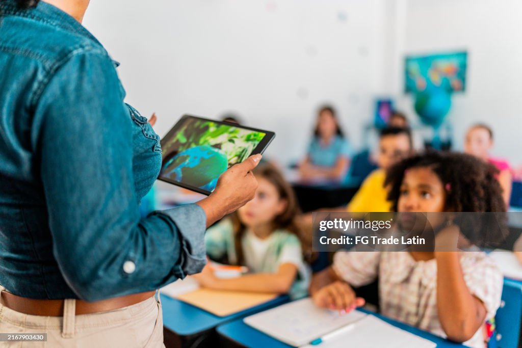 Mid adult teacher talking and using digital tablet during environment class at school