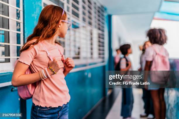 niña triste que mira a los estudiantes hablando y siendo excluida en la escuela - acoso escolar fotografías e imágenes de stock