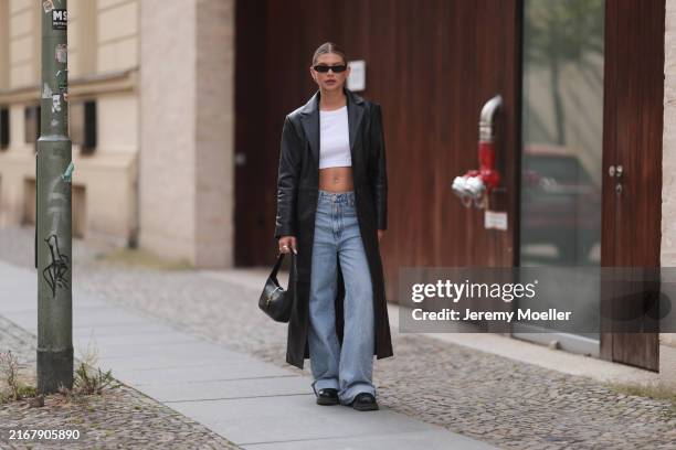 Sophia Geiss is seen wearing oval narrow black sunglasses from Saint Laurent, a silver nose ring, several silver hoop earrings, a calf-length black...