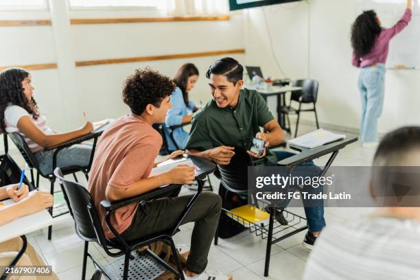 teenager sprechen und schauen sich während des unterrichts im klassenzimmer ein video auf dem handy an - sekundarschule stock-fotos und bilder