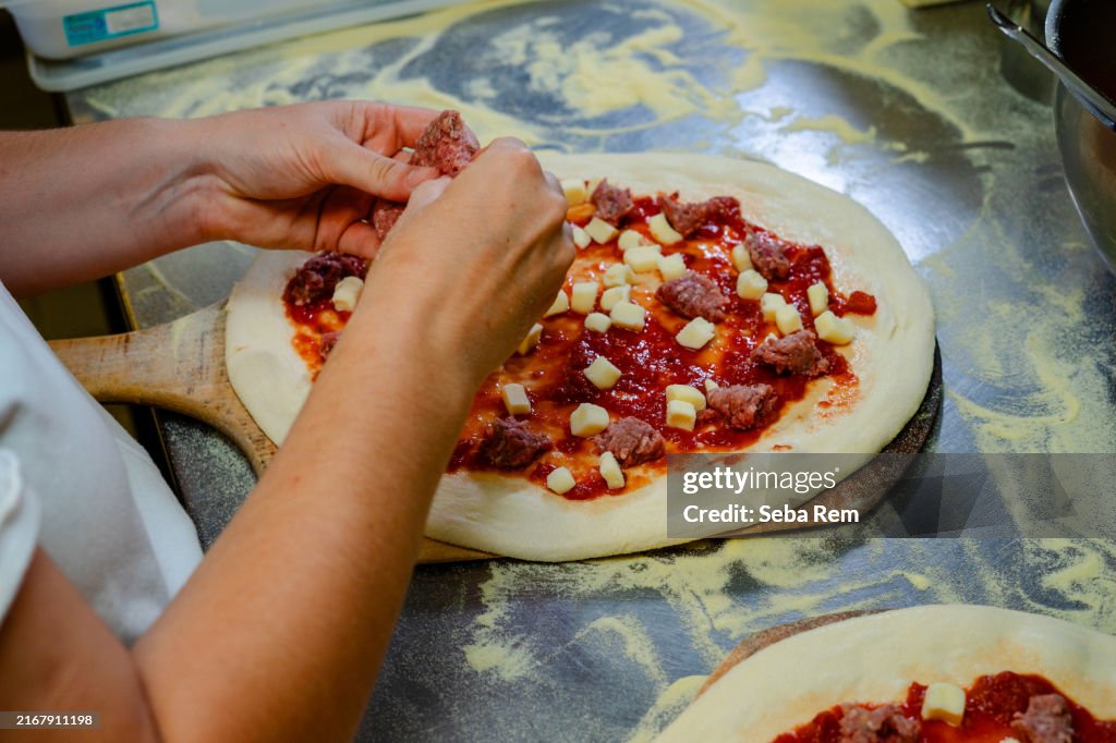 Artisanal pizza preparation: dough topped with tomato sauce, mozzarella, and sausage, ready for baking in a rustic kitchen