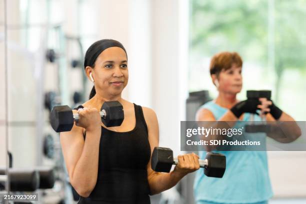 mid adult female personal trainer stands in front of her client to demonstrate different movements - weightlifting stock pictures, royalty-free photos & images