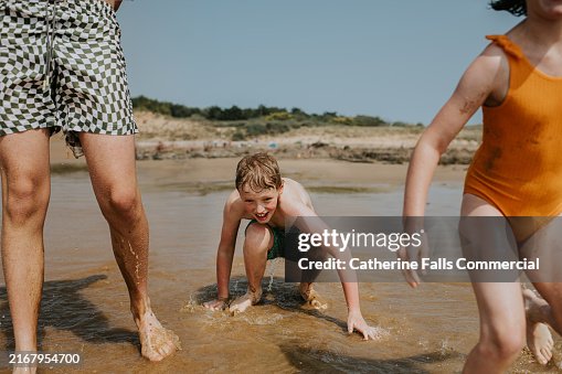 Children playing joyfully in shallow ocean water during a sunny day at the beach, capturing fun moments along the shoreline by the coast Children playing joyfully in shallow ocean water during a sunny day at the beach, capturing fun moments along the shoreline by the coast