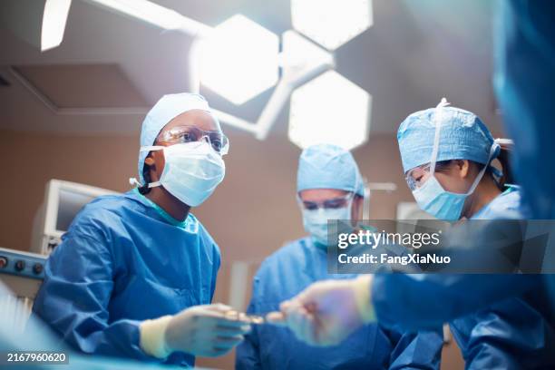 ethnie noire africain mid adulte femme médecin médecin chirurgien infirmière passant outil médical dans la salle d’opération chirurgie hôpital avec équipe médicale - chirurgien photos et images de collection