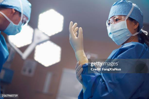 jeune femme asiatique chinois médecin chirurgien infirmière enfilant des gants chirurgicaux dans la salle d’opération de l’hôpital - masque de chirurgien photos et images de collection