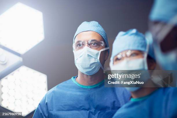 portrait of middle eastern multiracial mature man medical doctor surgeon nurse in operating room in hospital with surgical light and colleagues - chirurg stockfoto's en -beelden