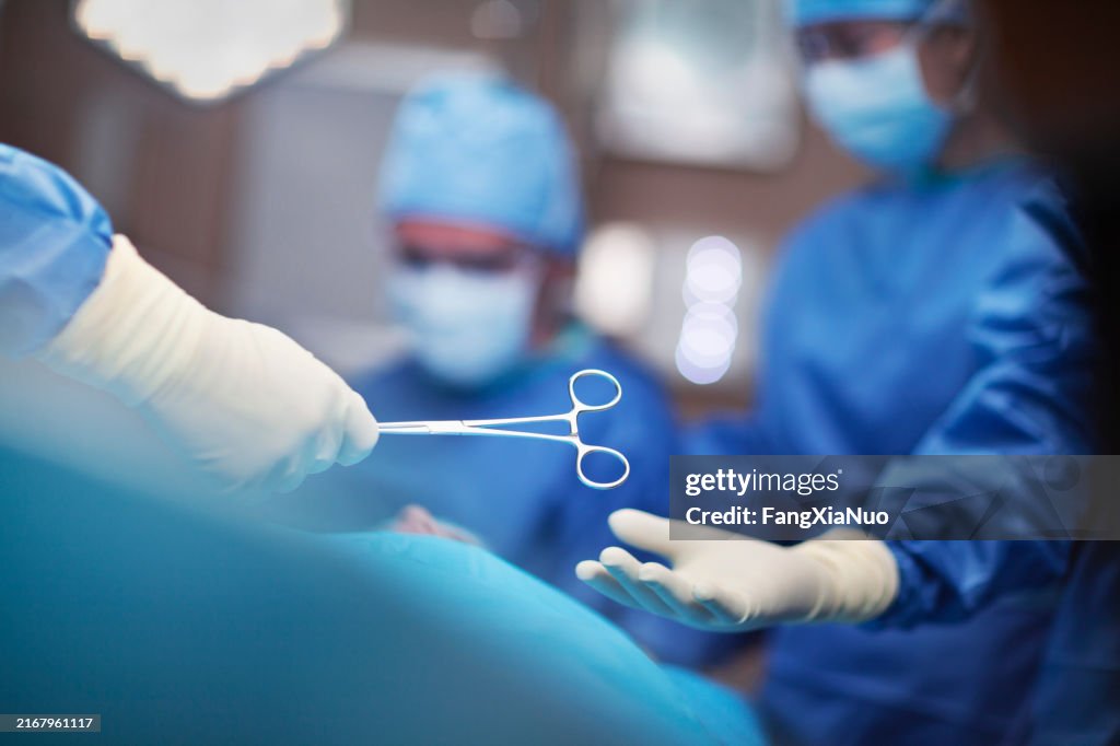 View of hands of doctor surgeon nurse passing medical tool in surgery operating room hospital with medical team