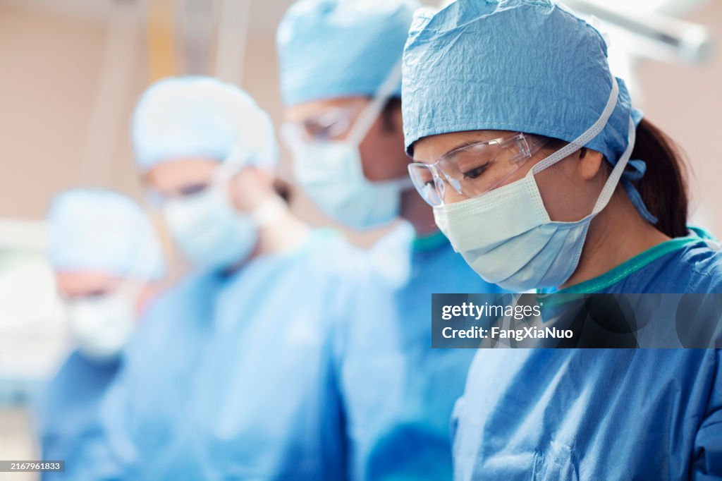 アジア系中国人中成人女性医師、外科医、看護師、病院の手術室で同僚のチームと患者を見下ろす