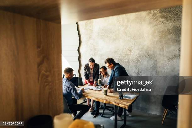four colleagues sitting at the table in the office - immobilienbüro stock-fotos und bilder